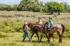 A woman leading two children on ponies on a sunny day at Gunstock Ranch in Oahu, Hawaii.