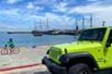 A neon green Jeep parked at the beach someone riding a bike passed it and a marina in the background on a sunny day in San Francisco.