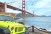 A bright green Jeep parked near the water with the Golden Gate Bridge in the background on a sunny day in San Francisco.