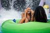 Two young women laughing and sitting in a giant green inner tube with water splashing all around them at Raging Waters Los Angeles.