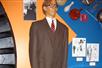 A very tall wax man in a brown suit and glasses with diagrams and old photos on the wall around him at Ripley's Believe It or Not! Orlando Odditorium.