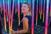A blonde woman walking through a room with rainbow light poles hanging front the ceiling at Mirror Maze in Orlando.