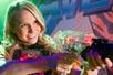 A blonde woman wearing a vest and holding up a laser gun while smiling at Ripley's Super Fun Park.
