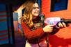 A woman in a red sweater and glasses smiling while playing laser tag at Ripley's Super Fun Park.