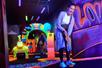 A woman smiling and playing mini-golf on a neon course at Rock of Ages Blacklight Mini Golf at the Mall of America.