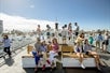 Several tourists onboard the San Diego Best of the Bay Harbor Cruise vessel, with some seated on benches while others standing just enjoying the beautiful views of the marina on a sunny day.