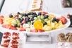 A large tray full of different fruits sitting on a table surrounded by different desserts on the San Francisco Lunch Cruise by Hornblower.