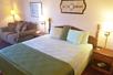 A green king size bed with side tables and a couch to the left with paintings on the wall at Scenic Hills Inn in Branson, Missouri, USA.