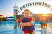 A young boy is all smiles as he poses in the blue life jacket he’s wearing as other children look on in the background.