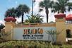 The sign for the Seralago Hotel & Suites Main Gate East with flowers and other landscaping in front of it on a sunny day in Kissimmee, FL.