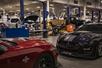 A red Shelby on the left and a blue/black on the right with a factory of car being built and worked on in the back.