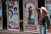 Trick Rider Emily wearing a black shirt with red accents and a white cowboy hat waving to the audience with posters in the background.