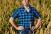 A man wearing a blue plaid flannel shirt in a cornfield from the Broadway musical Shucked in NYC, New York.