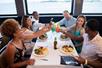 A group of friends cheering their drinks together over their lunch and smiling on the Signature Spirit of Baltimore Lunch Cruise.