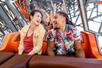 A young man and woman looking at each other and laughing while riding an orange roller coaster at Six Flags.
