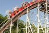 A large group of people excitedly raise their hands while riding the massive 4,200-foot wooden coaster, the Comet, as it hurtles downhill at Six Flags Great Escape.
