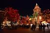 Wide shot of guests walking through Six Flags during Holiday in the Park with the trees and buildings decorated with Christmas lights at night.