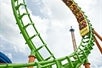 Several park-goers are thrilled as they experience the exhilarating ride of the 125-feet tall Boomerang coaster, with its green track, orange frame, and yellow cars looping against the backdrop of clouds on a cloudy day at Six Flags St. Louis.