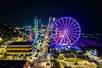 Aerial view of the Myrtle Beach SkyWheel glowing bright purple on a dark night with other city lights around it.