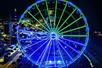 Aerial view of the Myrtle Beach SkyWheel at night with half of it glowing bright blue and the other half green.