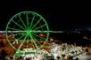 Aerial view of the SkyWheel in Panama City Beach at night with the lights on the wheel glowing green.