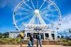 Three friends carrying their prizes and walking front of the SkyWheel at Panama City Beach on a sunny day with a bright blue sky overhead.