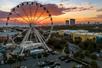 The SkyWheel at Panama City beach with an orangey-pink sunset in the background and several cars in the parking lot below.