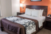 A hotel room with a white and brown queen beds, two nightstands with lamps, and an orange accent wall.