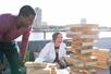 A man and woman laughing while playing Jenga on the desk of a cruise boat on a sunny day with the city of Chicago behind them.
