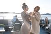 Two women in beige dressed standing together and laughing while cheering their drinks together on the Spirit of Norfolk Signature Brunch Cruise.