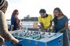 Friends laughing and playing foosball on the deck of a cruise boat on a sunny day on the Spirit of Norfolk Signature Brunch Cruise.