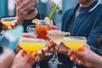 Close up of a group of people cheering their brightly colored cocktails together.