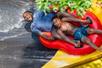 A father and son tightly grip the handles as they ride in a red inflatable tube, plunging down from Dragon's Den at Splish Splash.
