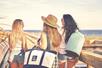 Three woman carrying IceMule Coolers in a variety of sizes to the beach on a sunny day.