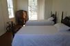 A room with several windows, two wooden vintage beds, and an armoire for guests at Felicity Plantation in Vacherie, LA