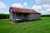 An old worn building with wooden slat walls, and a rusted tin roof on a sunny day at the Felicity Plantation in Vacherie, LA