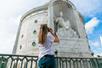 A woman in a white shirt with long hair taking a photo of the Italian Benevolent Society Tomb on a sunny day.