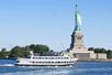 A white cruise boat with tourists standing on it's top deck sailing past the Statue of Liberty on a sunny day on the Statue of Liberty & Ellis Island with Round-trip Ferry.