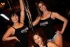 A group of three women in black tank top posed around a stripped pole for the photo at the Stripper 101 - Pole Dancing Class.