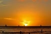 People surf and sail while the sun sets in Waikiki, Hawaii.