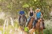 Three riders on horseback smiling as they ride along the trails at Gunstock Ranch in Oahu - Kahuku, HI