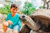 A young boy in a bright blue shirt smiling and petting a Giant Tortoise at ZooTampa at Lowry Park.
