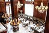 View looking down on a dining room with dark wooden walls, large windows, several chandeliers, and several tables and booths.