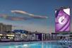 The Boulevard Pool, a large outdoor swimming pool with purple lounge chairs around it, at night with a sign for the The Cosmopolitan of Las Vegas over it.