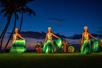 Three hula dancers standing in front of a band on the beach at sunset at The Feast at Mokapu Luau in Wailea, Hawaii, USA.