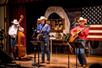 Musicians in cowboy hats and shirts performing on stage at The Great American Chuckwagon Dinner Show.