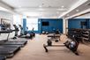 A fitness center with cardio equipment on the left, weights on the right in front of a mirror wall, and a window on a blue accent wall.