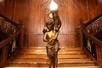 A gold statue of a cherub in the middle of a large wooden staircase at the Titanic - The Artifact Exhibition.