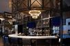 The lobby bar at The Porter Portland with a curved white countertop with a chandelier over head and a wall of alcohol behind it.