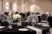 A banquet room full of black cloth covered tables set with plates and glasses and flowers in the middle.